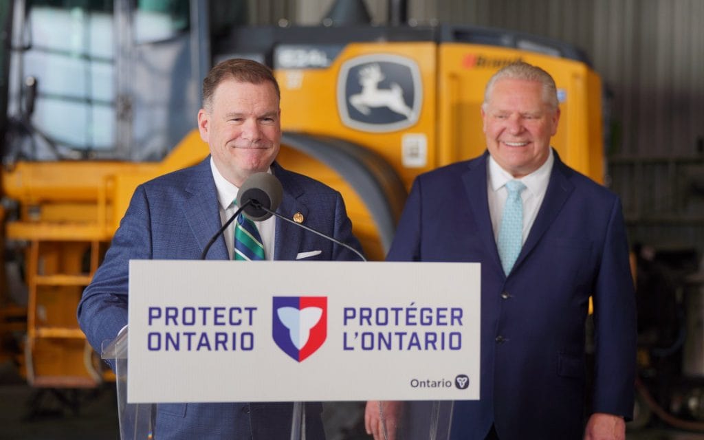 Two men stand behind a lectern that says "Protect Ontario" on it in English and French.