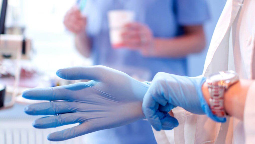 Close up of female doctor's hands putting on blue sterilized surgical gloves in the medical clinic.