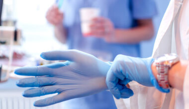 Close up of female doctor's hands putting on blue sterilized surgical gloves in the medical clinic.
