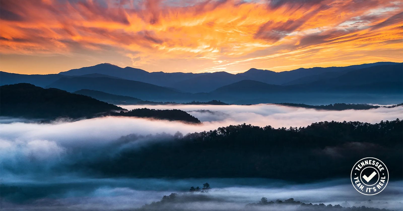 Colorful sunrise sky with dramatic orange clouds above misty mountains and forested hills; fog blankets the valleys. A "Tennessee, Lean Into It" logo appears in the lower right corner.
