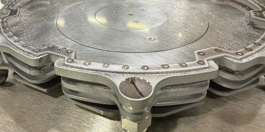 Close-up of a metallic engine component with cooling fins and a circular opening.