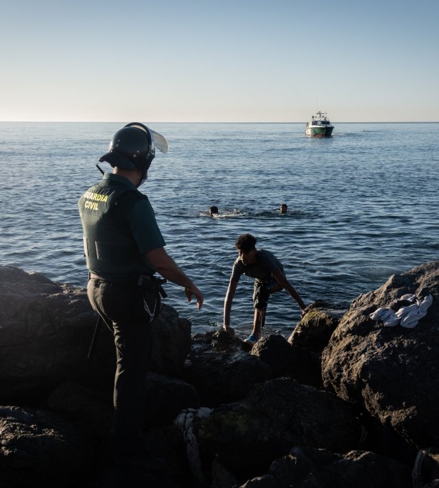 CEUTA, SPAIN - MAY 19: A young migrant who has crossed the border between Spain and Morocco by swimming along the Tarajal beach, steps out of the sea towards a member of the Civil Guard, before he is returned to Morocco on May 19, 2021 in Ceuta, Spain. After a diplomatic conflict between Spain and Morocco, thousands of migrants have taken advantage of the little Moroccan police activity to cross the border, mainly by swimming. This has caused a migration crisis, with the entry of more than 8000 migrants from the African country. (Photo by Joan Amengual/VIEWpress/Corbis via Getty Image )