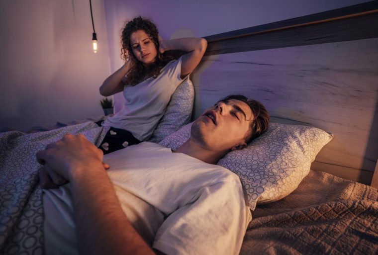 Young woman covering her ears while her boyfriend snoring in bed