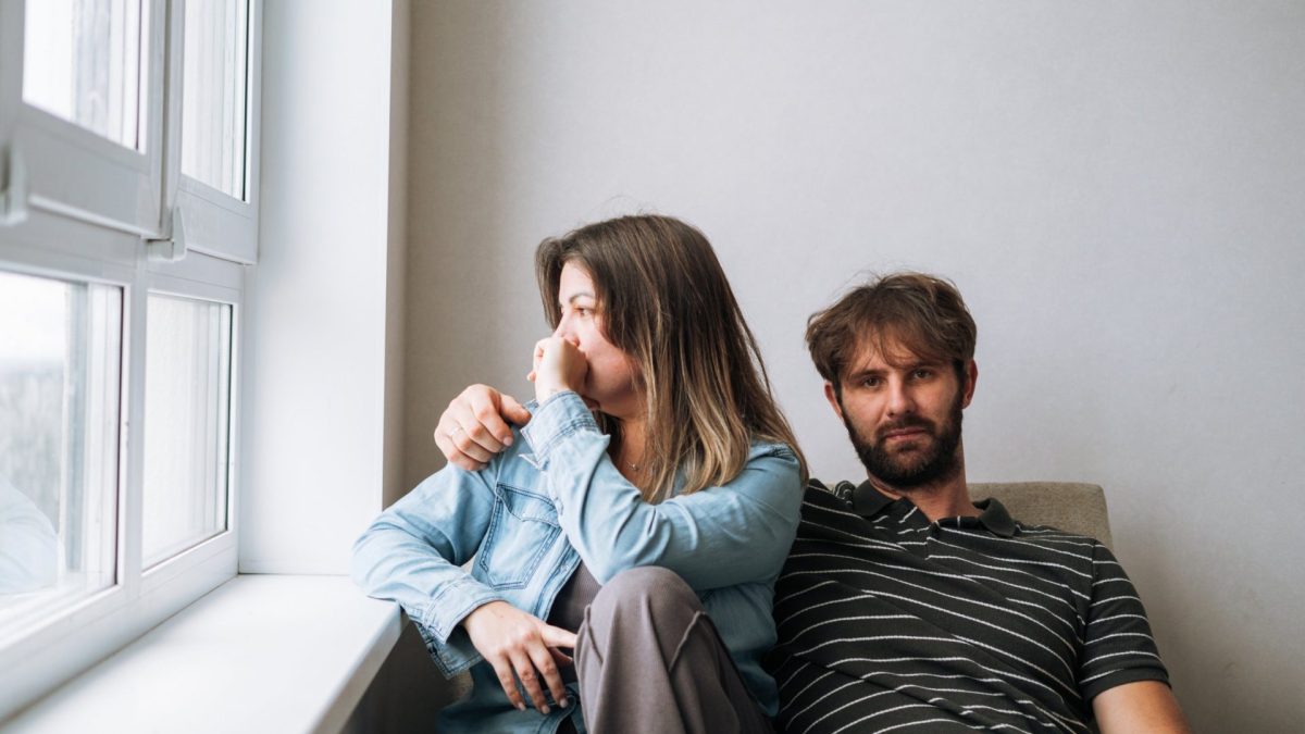A married couple sitting in silence, looking in opposite directions. The image captures the concept of female loneliness within a marriage, emotional disconnection, and relationship problems. Symbolizes quiet desperation and isolation at home