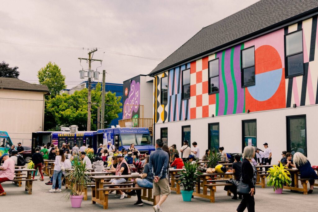 People eat at picnic tables next to a mural.