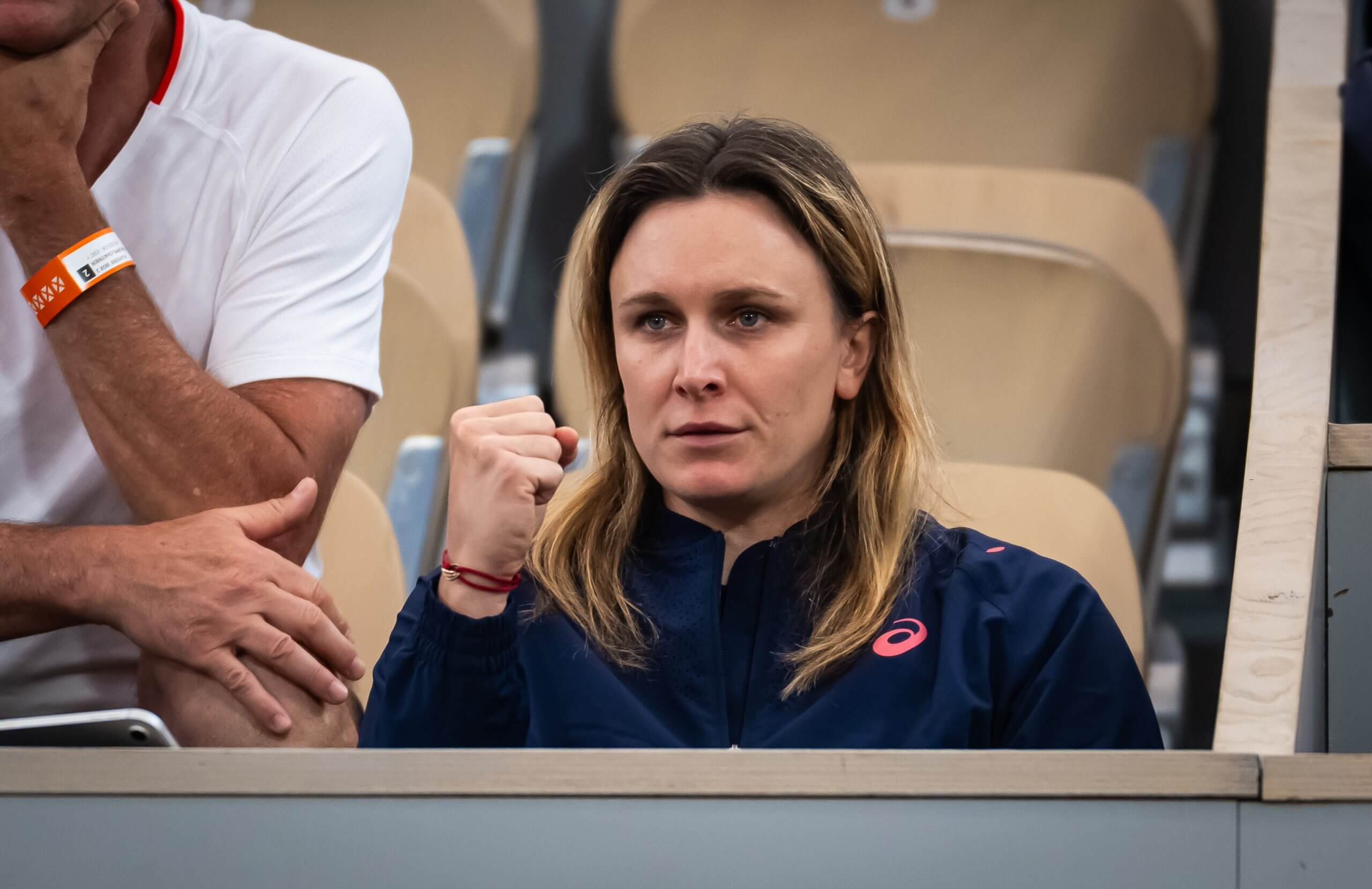 Sandra Zaniewska looks on with a pumped fist in celebration, sitting in a tennis stadium.