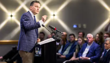 Evan Solomon speaks on stage with bright lights behind him.