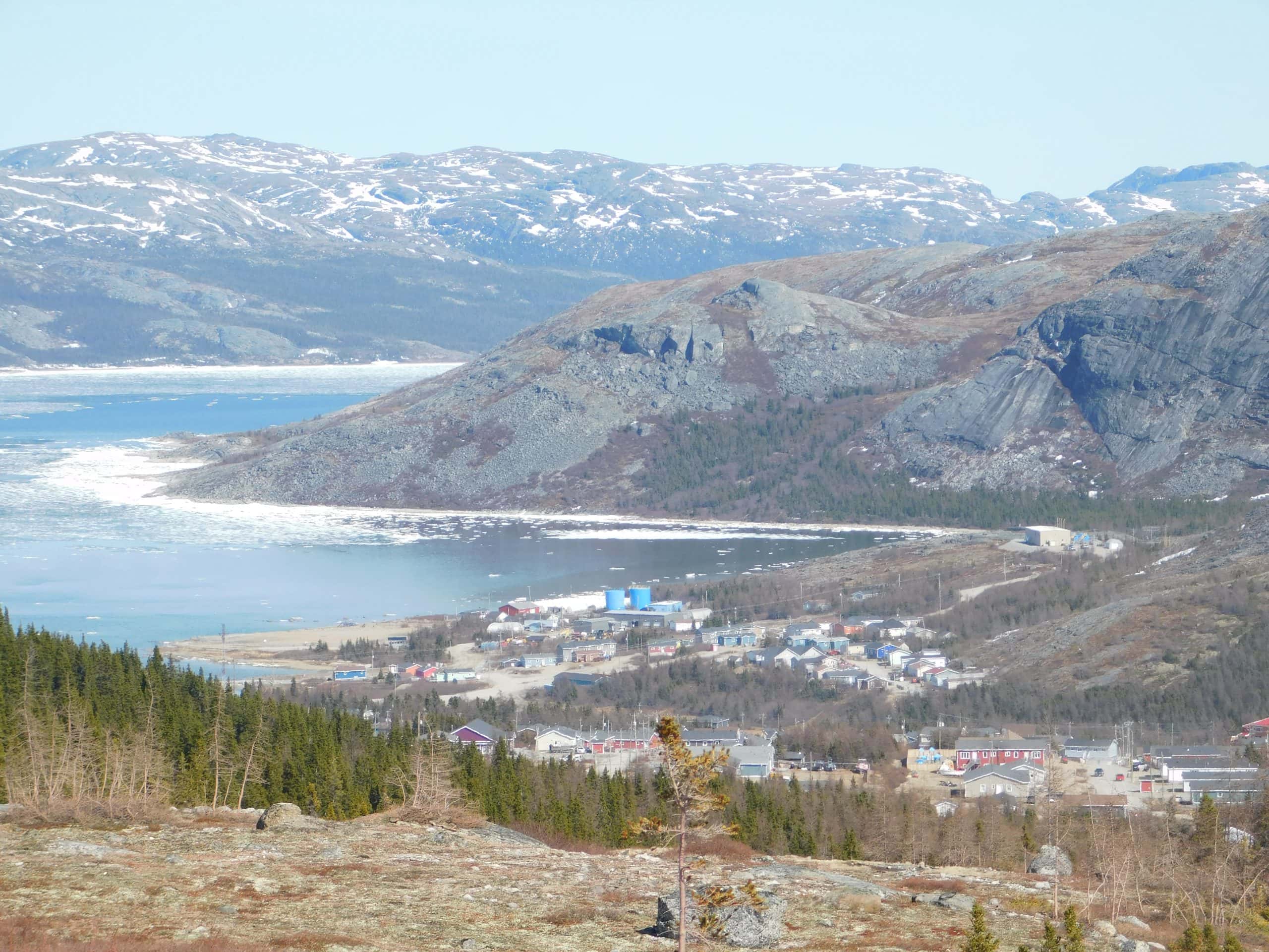 The Inuit community of Nain, Labrador, is seen from above. It is nestled beside a cove along a rocky shoreline.