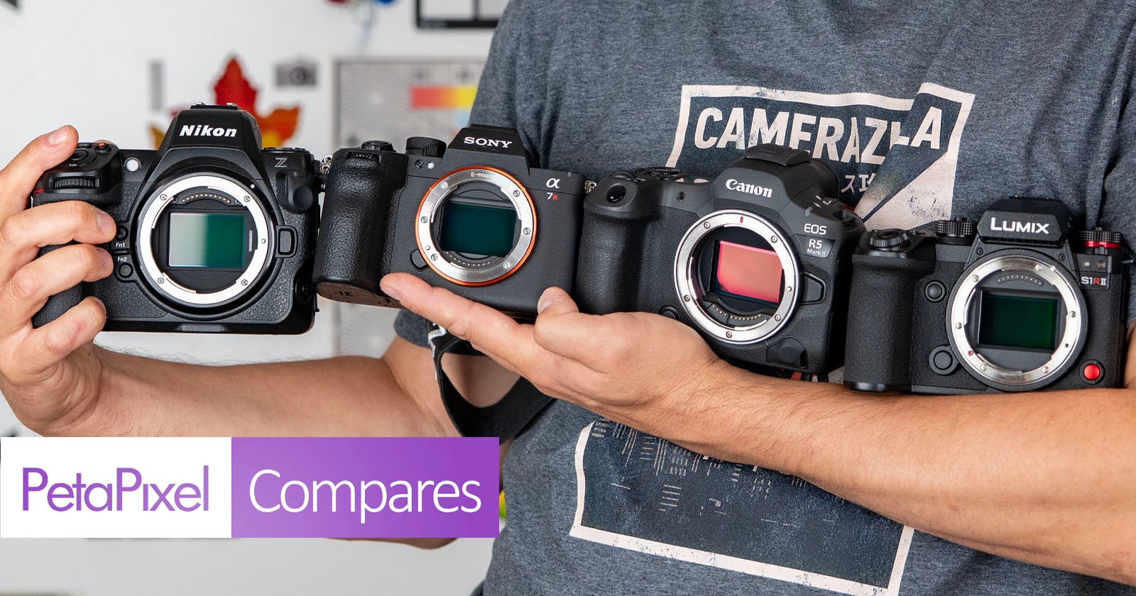 Person holding four mirrorless cameras—Nikon, Sony, Canon, and Lumix—side by side, with no lenses attached. "PetaPixel Compares" text is at the bottom left corner.