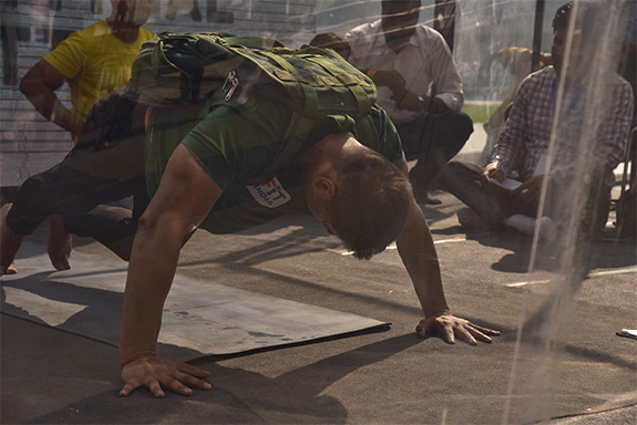 a man wearing a green t shirt performs a push up with a backpack on