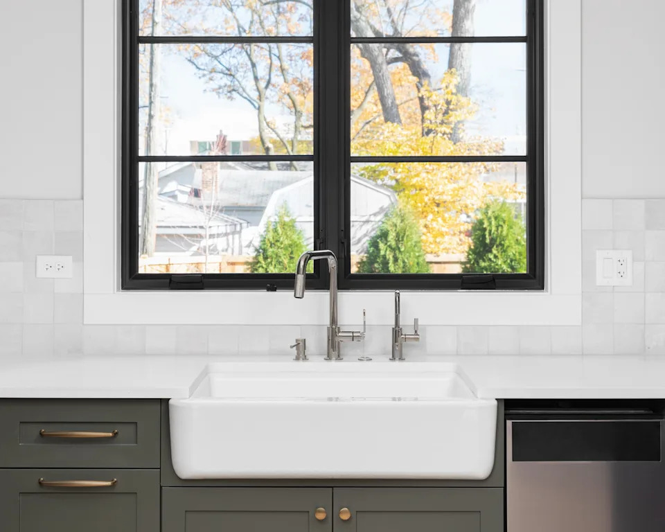 A modern kitchen sink with a sleek faucet beneath a window showing a view of trees
