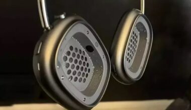 Close-up of grey over-ear studio headphones with perforated circular ear cups and metallic rims against a dark background.