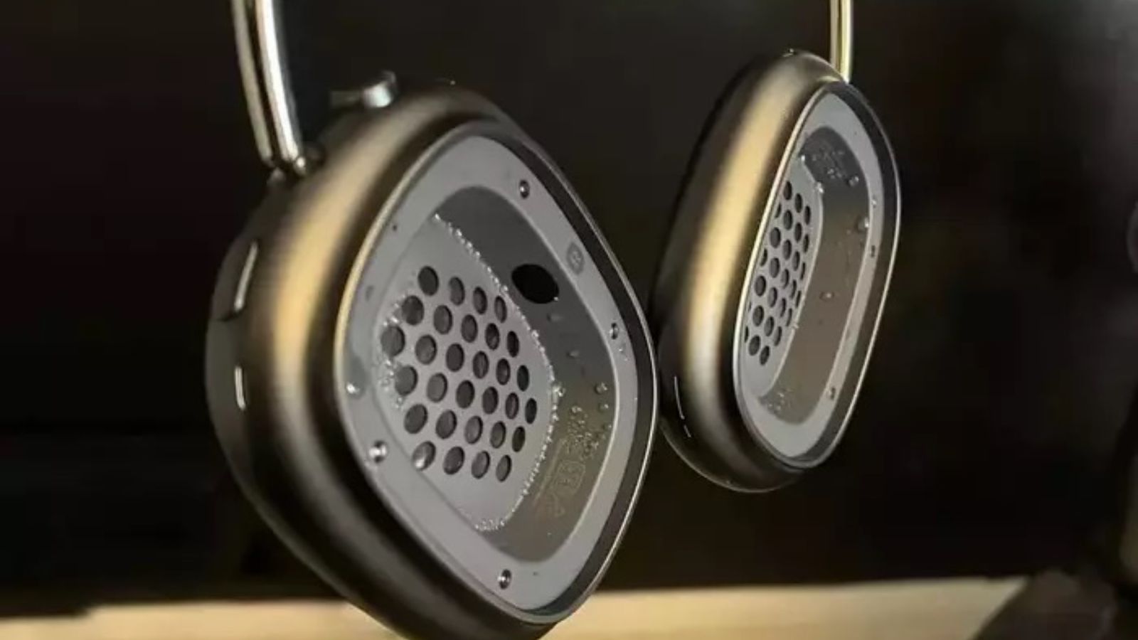 Close-up of grey over-ear studio headphones with perforated circular ear cups and metallic rims against a dark background.