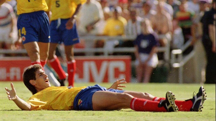 A soccer player is lying on the ground, his head and hands held up in disappointment.