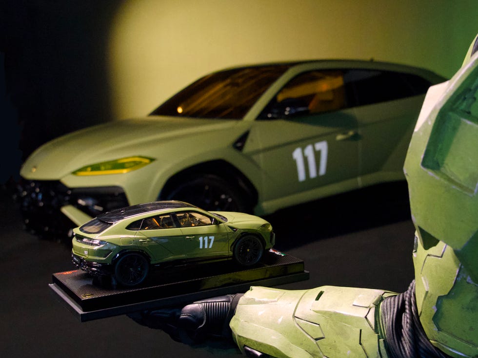 A green toy car model on a display base, held by a Master Chief in armor, with a matching green vehicle in the background. A green toy car model on a display base, held by a Master Chief in armor, with a matching green vehicle in the background.