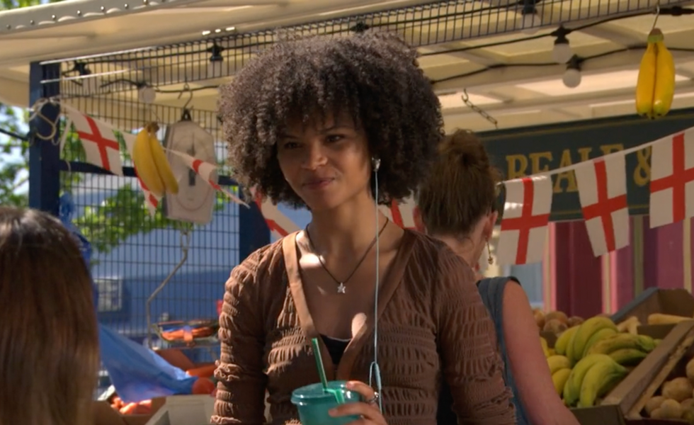 Jasmine, EastEnders woman holding a drink cup at an outdoor market stall