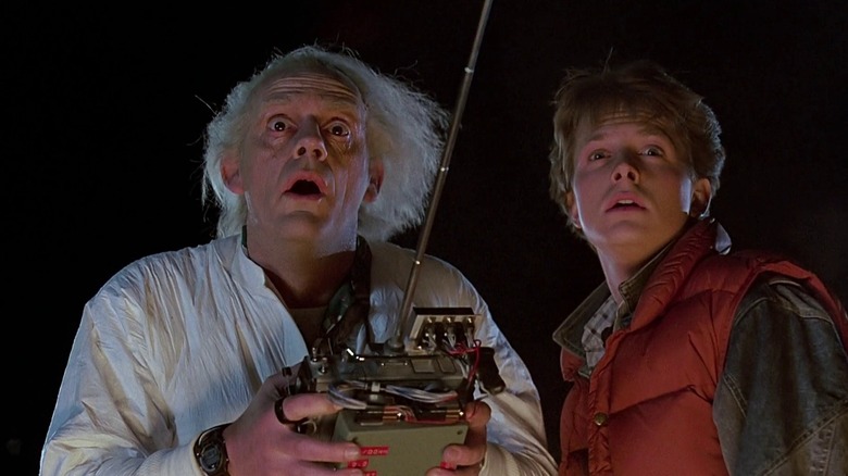 Michael J. Fox as Marty McFly and Christopher Lloyd as Dr. Emmett Brown in Back to the Future, standing next to each other at night and looking off in amazement as Dr. Brown holds the time travel device.