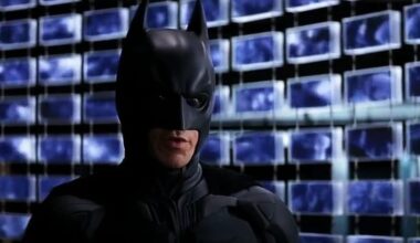 Batman stands in front of computer screens.