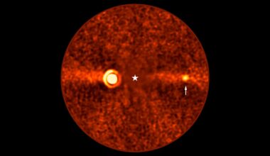 Orange-hued, grainy circular image of a star at the center with a glowing ring to the left and a smaller bright spot to the right, indicated by an arrow. The background is dark with scattered noise.