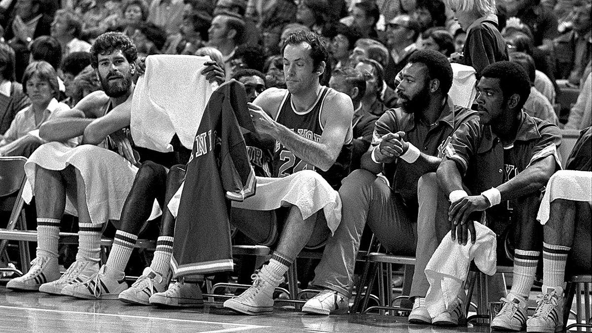 Bill Bradley puts on his warmup jersey while seated on the bench during an NBA game against the Denver Nuggets.