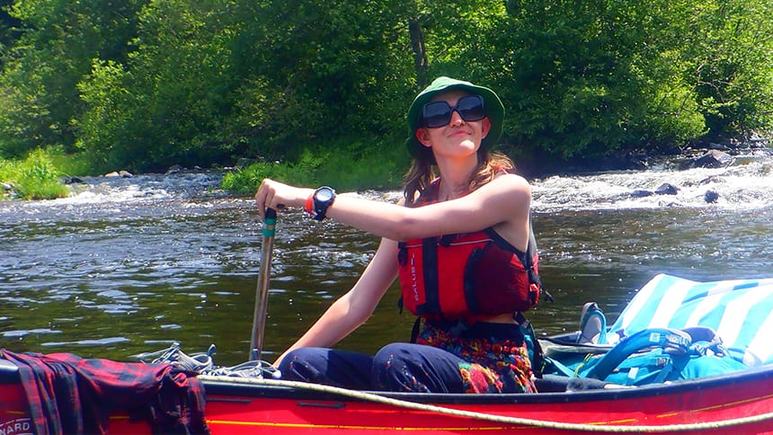 A teen rides in a canoe on a river.