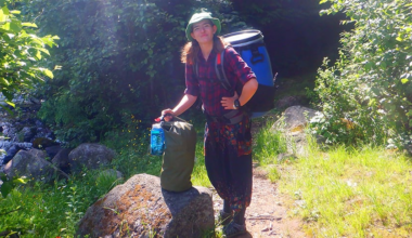 A teenager holding two backpacks on a hiking trail.