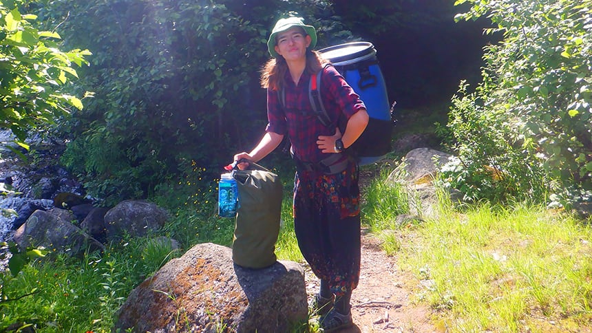 A teenager holding two backpacks on a hiking trail.