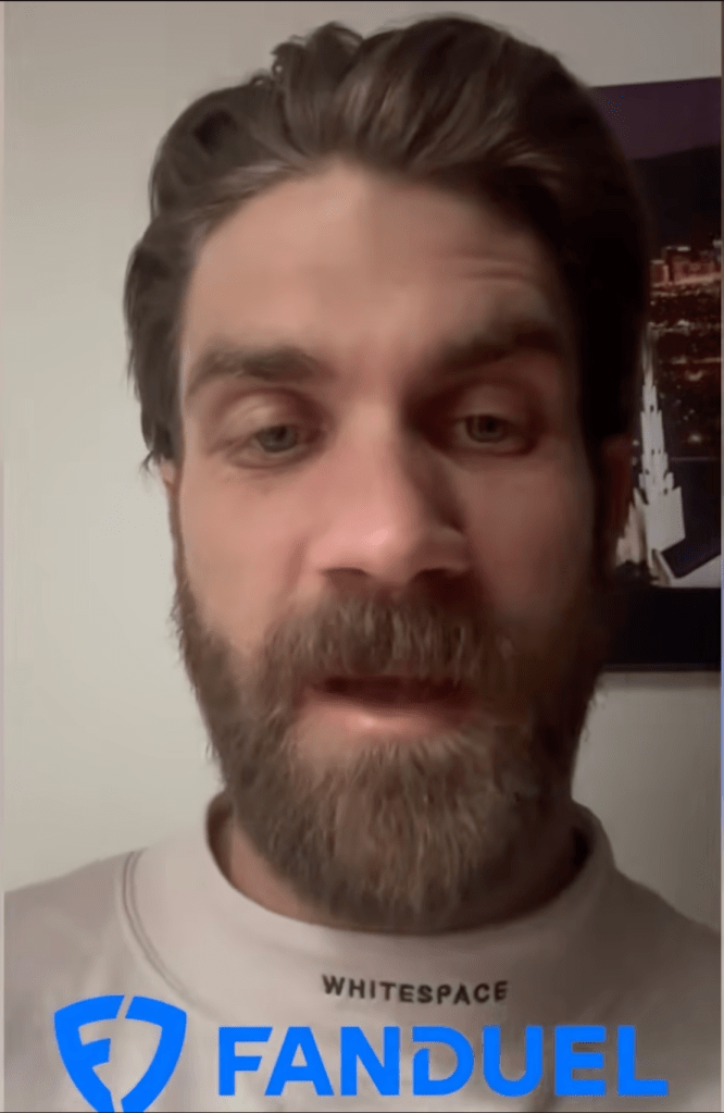Bryce Harper with a beard wearing a white sweatshirt and a FanDuel logo.