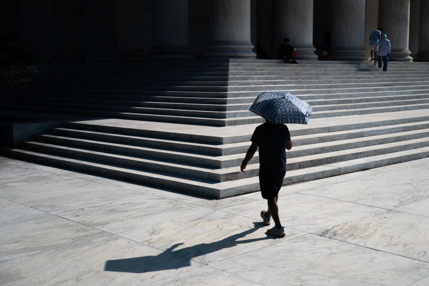 A visitor walks up the front steps of the Jefferson Memorial while carrying a sun umbrella during an extreme heat advisory, on Thursday, in Washington.