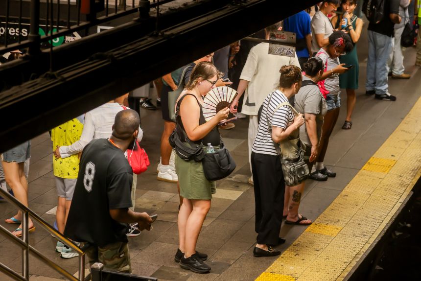 A commuter holds a handheld fan and carries a water bottle while waiting for a train at Union Square station during high temperatures in New York, on Thursday.