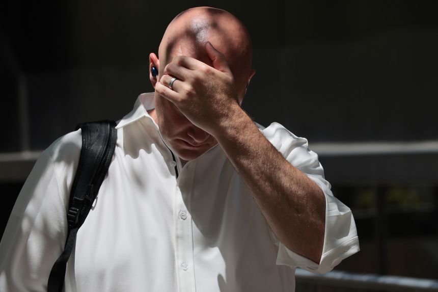 A person wipes sweat off their head while standing under the shade of a tree on Thursday in New York City.