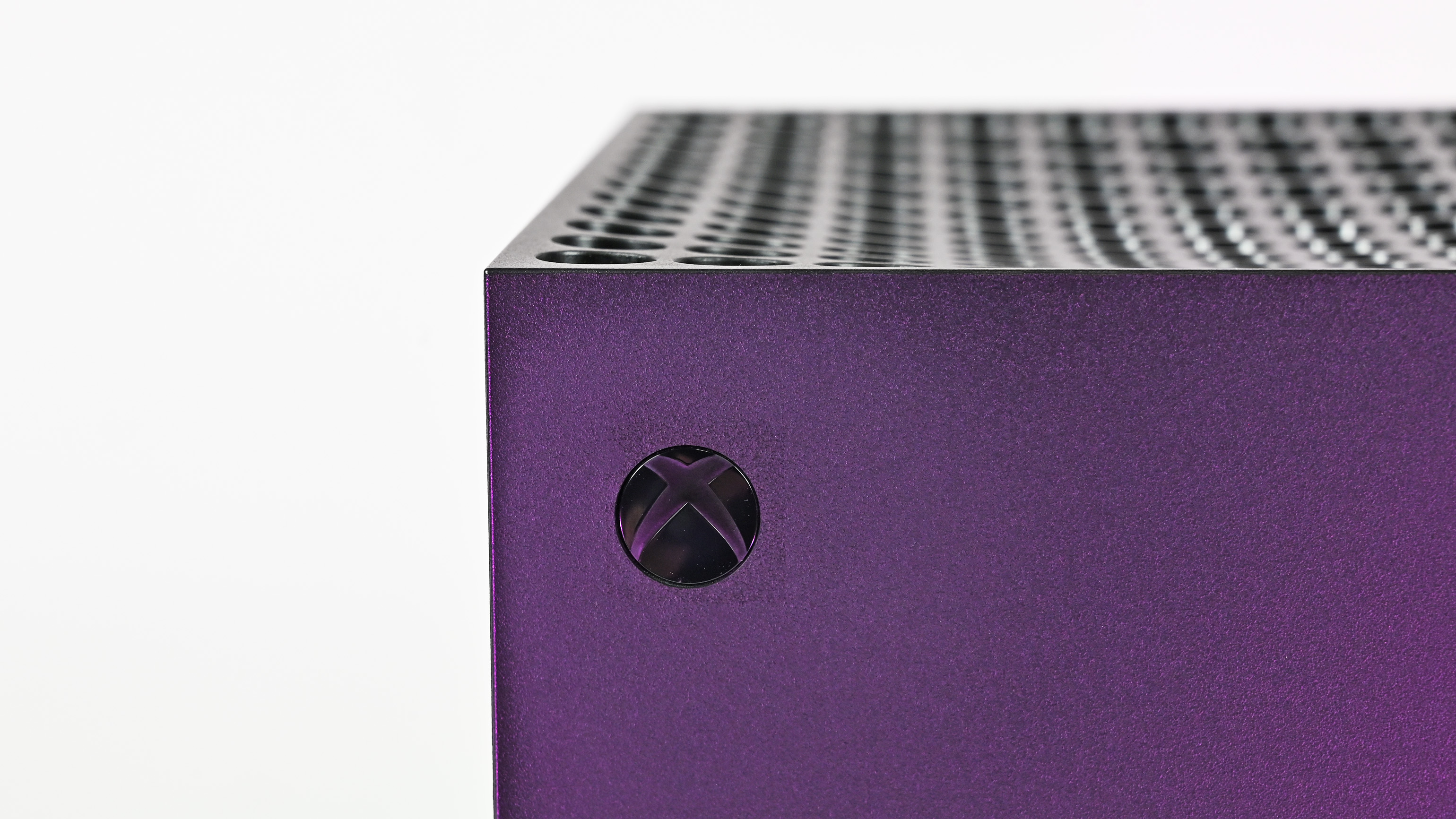 Macro shot of the circular Xbox logo power button on the corner of the console, under a purple metallic sheen.