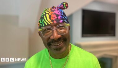 Mr Motivator, who is weaing a bright green t-shirt and a multi-coloured bandana. He also wears a gold chain. He is smiling in the photo.