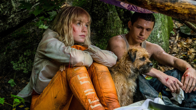 Daisy Ridley as Viola and Tom Holland as Todd huddle by a tree with a dog in Chaos Walking