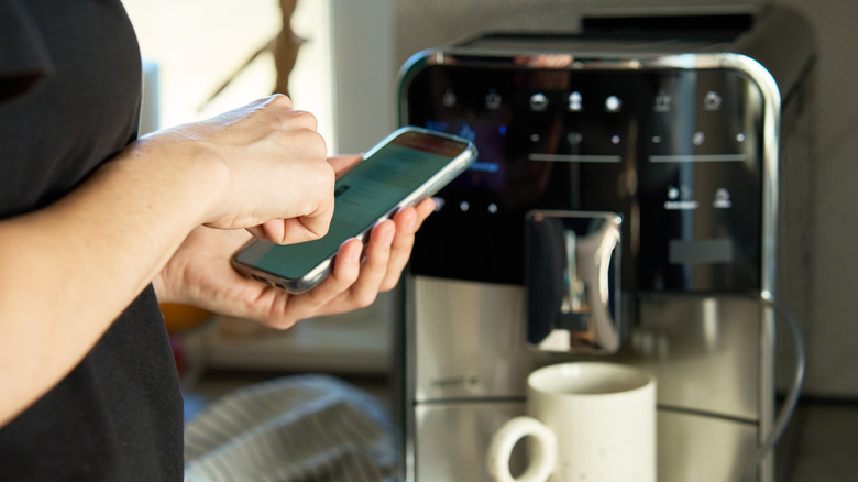 A person using their smartphone in front of a coffee maker