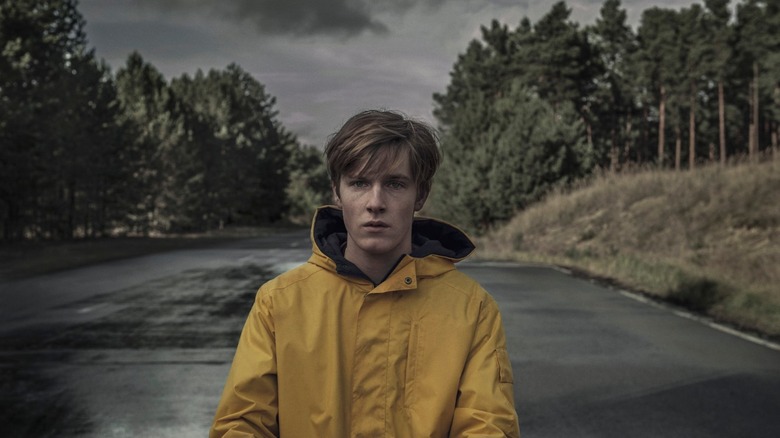Louis Hofmann as Jonas Kahnwald, wearing a rain coat in the road in Dark.