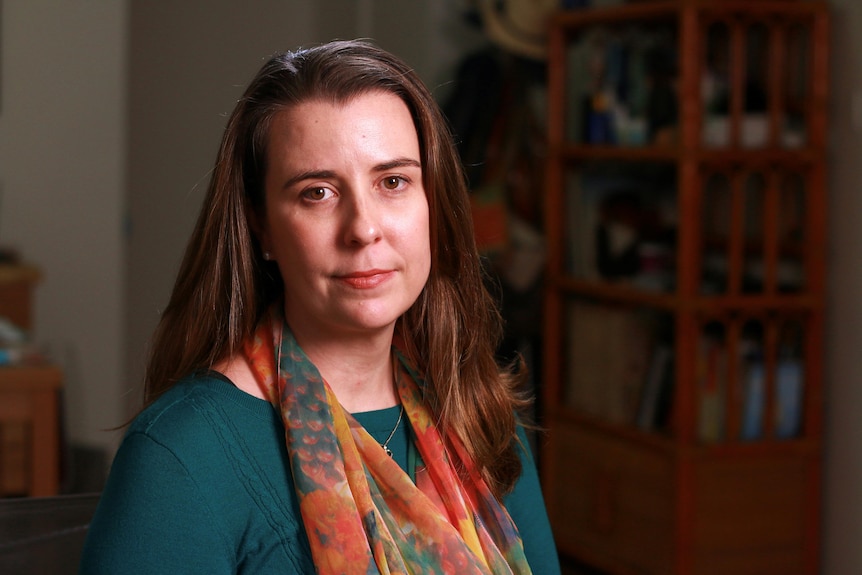 A woman with long, dark hair wears a scarf and stands in a study.