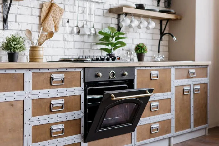 Stylish kitchen with brick wall, industrial cabinets, open oven, cookware, potted plants, and hanging utensils
