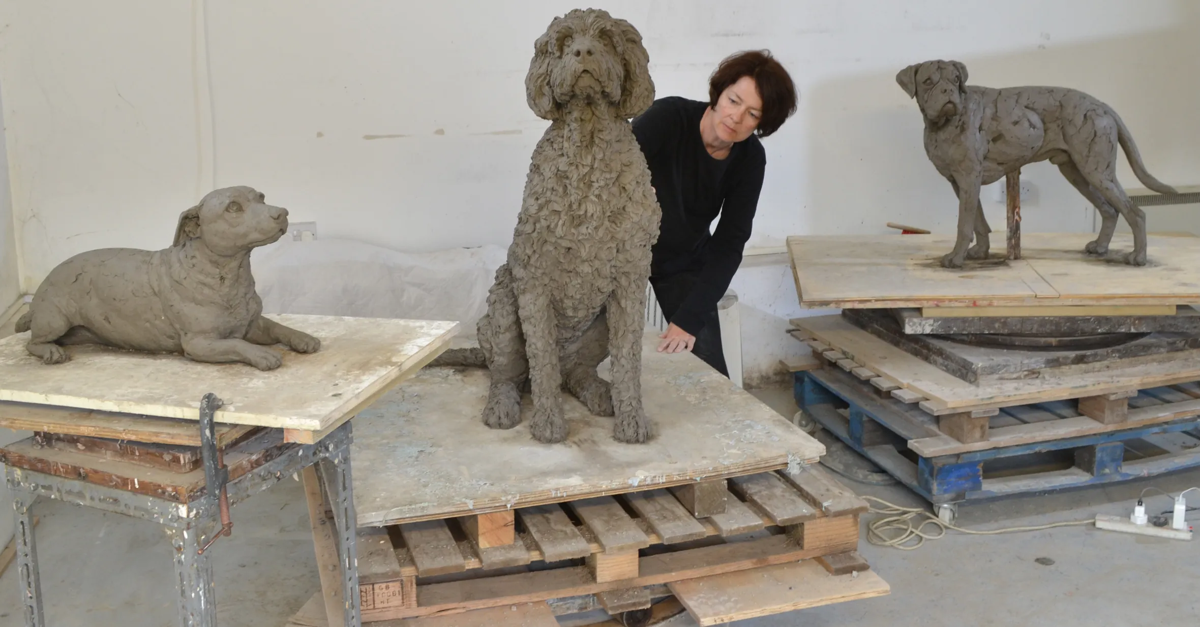 Tanya Russell working on clay sculptures of a Labradoodle, Boxer, and Jack Russell Terrier.