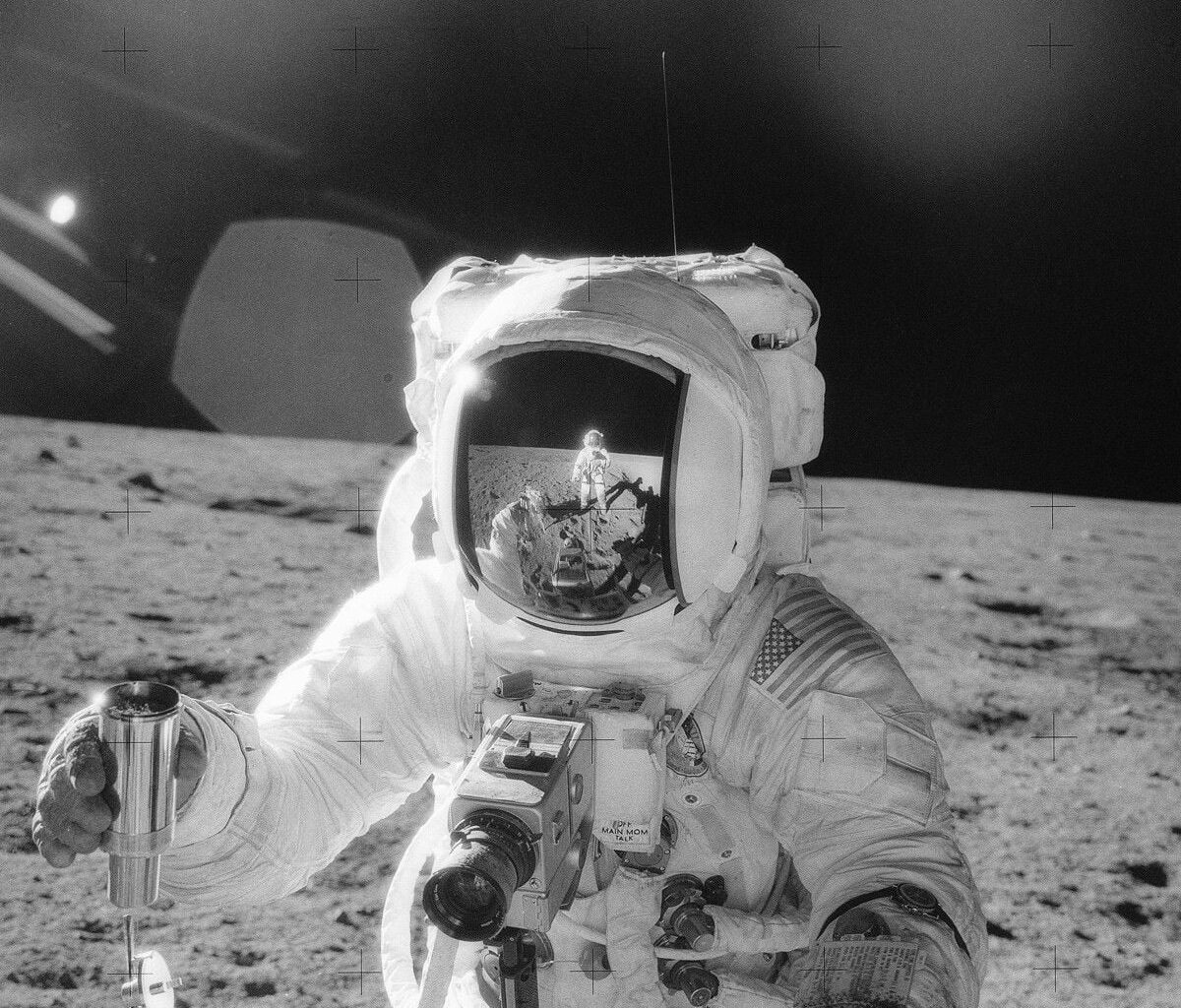 NASA's Apollo 12 mission photo shows an astronaut on the Moon's surface holding a container of lunar soil, with the other astronaut reflected in his helmet visor (Credit : NASA)
