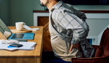 Man holding lower back in pain while sitting at a desk, struggling with poor posture during remote work