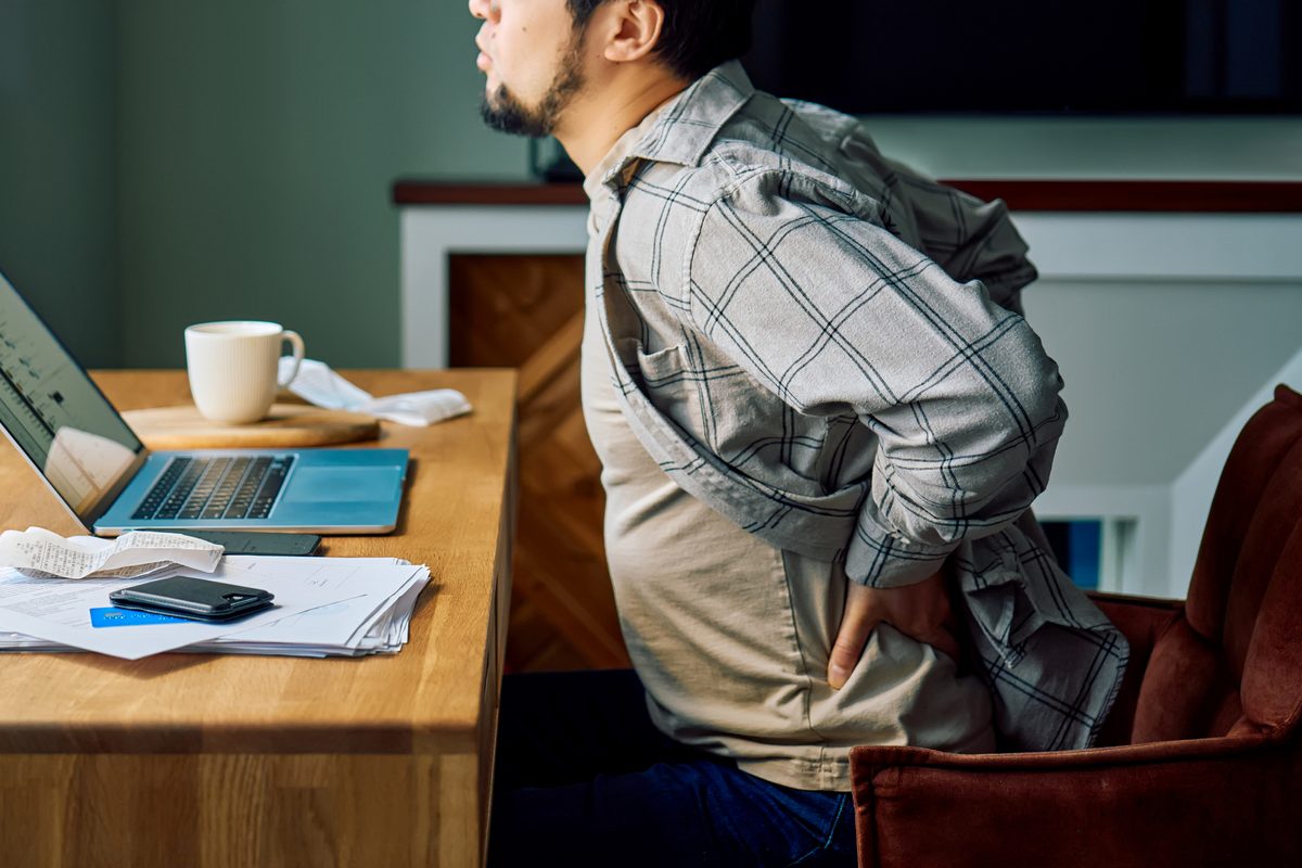 Man holding lower back in pain while sitting at a desk, struggling with poor posture during remote work