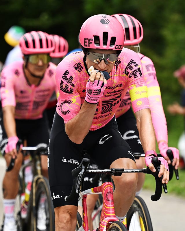 Cyclists in pink jerseys riding on a road, one is eating while others focus ahead. Cyclists in pink jerseys riding on a road, one is eating while others focus ahead.