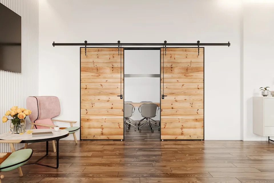 Modern office with sliding wooden barn doors, revealing a conference room with chairs, a pink chair, table with flowers, and a side cabinet in view