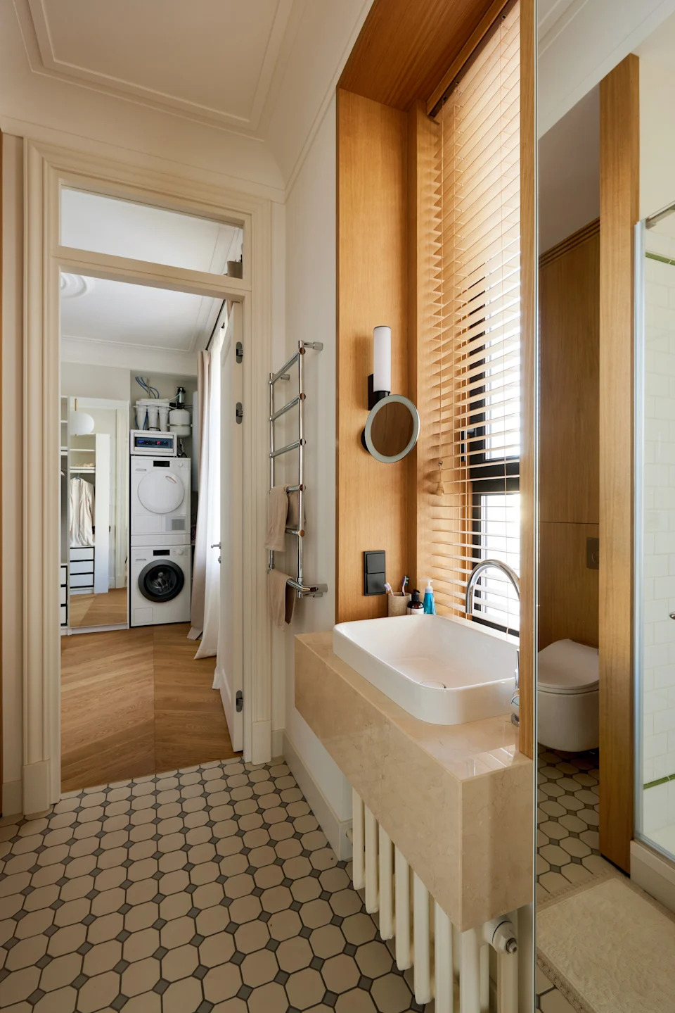 Bathroom with a modern sink, large mirror, and towel rack. Nearby, a hallway leads to a compact laundry area with a stacked washer and dryer