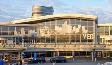 Exterior view of Edmonton International Airport departures terminal, featuring a large glass facade with a city skyline graphic and the letters “YEG” displayed at sunset.