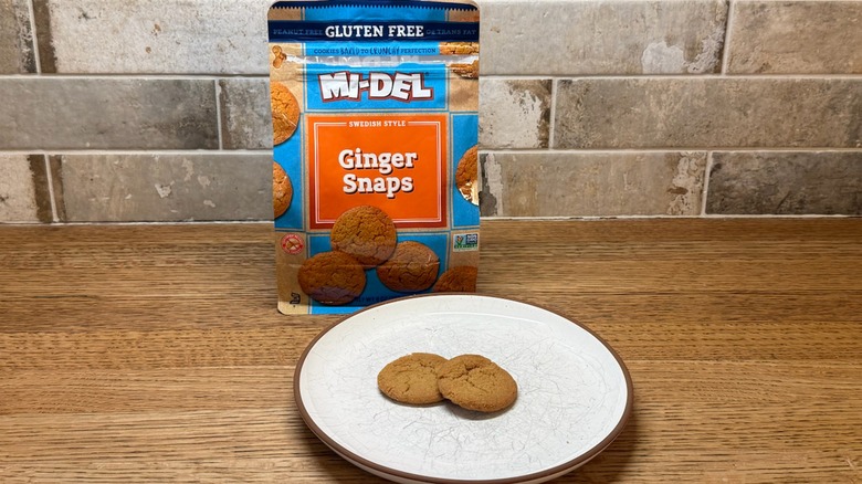 Mi-Del Ginger Snaps cookies in a bag with two cookies on a plate in front of the bag on a wooden counter