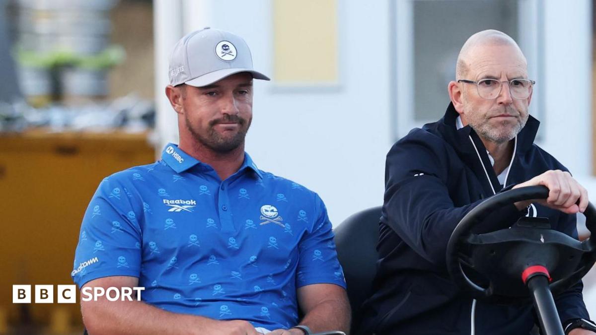 Bryson DeChambeau is driven on a buggy by an Open rules official