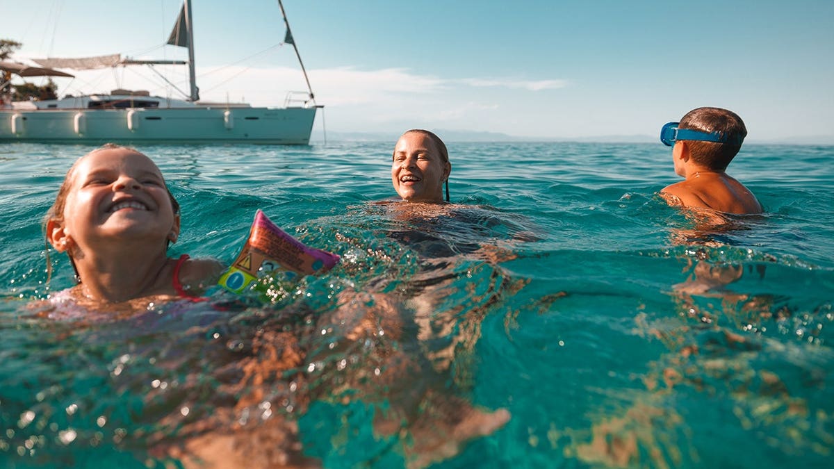 Mother, daughter and son swim in clear turquoise sea beside a rented boat.