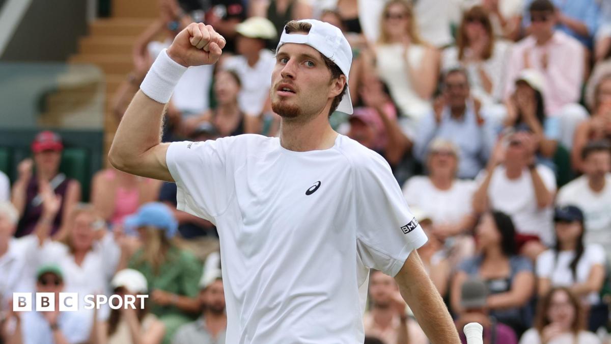 Toby Samuel wearing a white tennis shirt and baseball cap backwards pumps his fist towards the sky